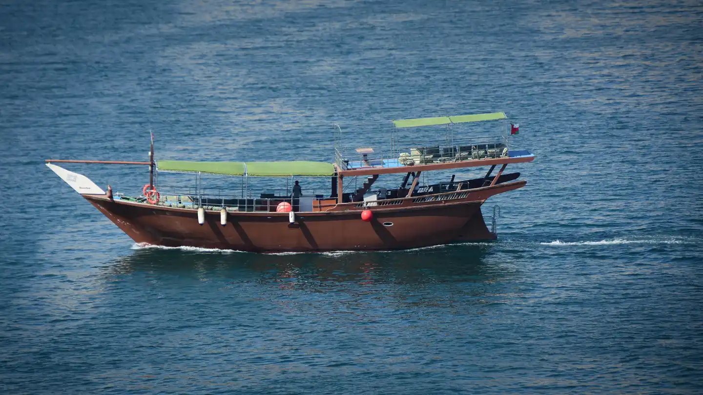 The comfortable shaded upper deck of a traditional Omani dhow, featuring colorful cushions, where a family relaxes during their Musandam cruise.